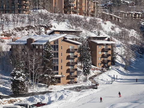 Ski-in location nestled at the base of groomed slopes, surrounded by snow-dusted pines and hillside lodges in a vibrant winter resort village.