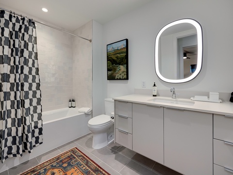 Sleek and modern, your bathroom features a spa-like tub, crisp white counters, and a backlit mirror that makes every morning feel fresh and bright.
