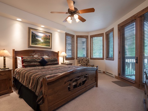 Step into your serene mountain retreat, where rustic charm meets comfort. Sink into the plush bed, warmed by soft lighting and a gentle ceiling fan, while views of nature peek through wooden blinds.