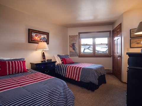 Cozy bedroom with twin beds dressed in nautical red-white-and-blue linens, perfect for kids or friends. Natural light, warm décor, and plenty of storage make your mountain getaway comfortable.