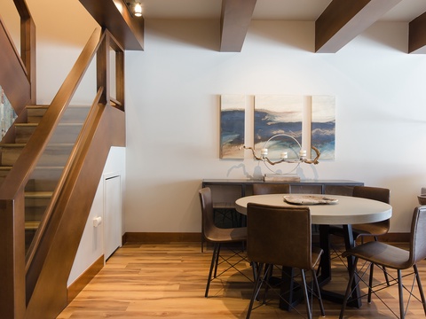 Gather around the stylish dining table beneath striking architectural beams and coastal-inspired artwork. Warm wood tones and modern design create your perfect space for memorable meals and conversation.