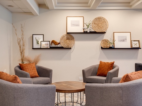 Relax in your cozy communal lounge featuring plush gray seating, warm burnt-orange accents, and thoughtfully curated wall shelves—perfect for unwinding with fellow travelers.