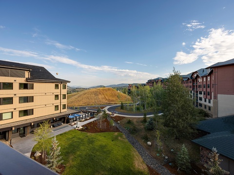 The property sits in a scenic mountain valley, surrounded by natural landscaping and neighboring buildings, with distant peaks visible under open skies.