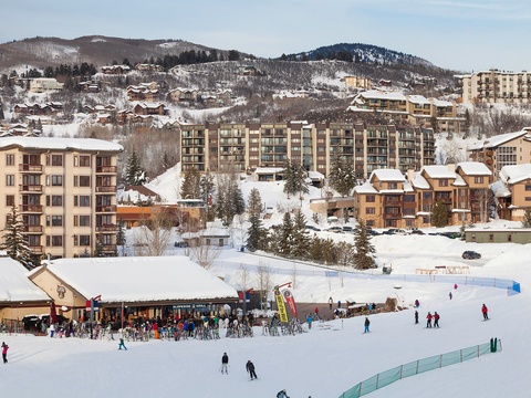 A vibrant winter resort area with ski slopes, lodges, and alpine village buildings nestled among snow-covered mountains and evergreen trees.