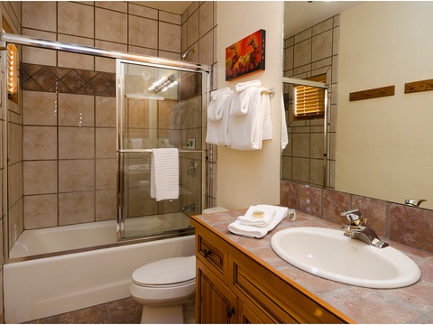 Step into your private bathroom featuring a tiled shower-tub combo, fresh towels, and warm wood accents. Everything you need to refresh and recharge after a day of adventure.