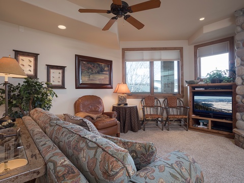 Settle into this warm living space with plush seating, a crackling stone fireplace, and large windows framing peaceful views—your perfect retreat for cozy evenings.