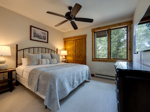 Unwind in your peaceful bedroom, where soft linens and natural light from large windows invite restful sleep. A ceiling fan keeps you cool while you enjoy views of lush greenery just outside.