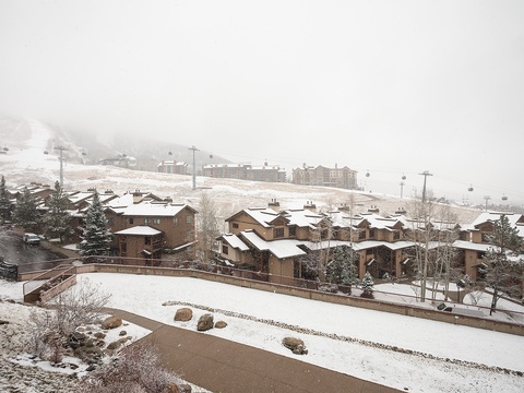 A snowy ski village nestled in the mountains, with gondola lifts ascending through the fog toward snow-covered slopes and rustic alpine lodges.