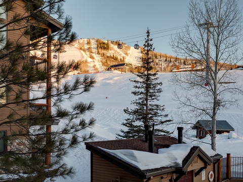 A ski-in property nestled at the base of pristine slopes, with gondolas overhead and snow-blanketed trails winding through evergreens, offering direct access to winter adventures.