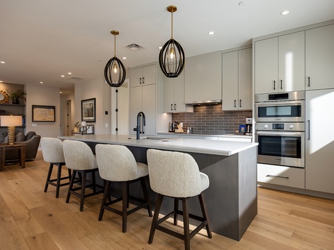 Step into your beautifully designed open kitchen where sleek white cabinetry meets warm wood floors and modern pendant lighting. Gather around the spacious island with seating for four, perfect for morning coffee or evening conversations.