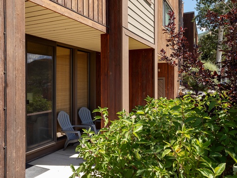 A contemporary alpine retreat featuring warm wood tones and private outdoor spaces, nestled among lush greenery with mountain views visible from the doorway.