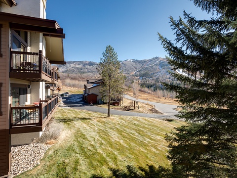 Mountain-framed property exterior with balconies overlooking a scenic valley, evergreen trees, and neighboring buildings in a peaceful neighborhood setting.