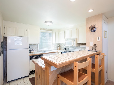 Your fully-equipped kitchen features white cabinetry, tile countertops, and a convenient breakfast bar perfect for casual meals and morning coffee together.