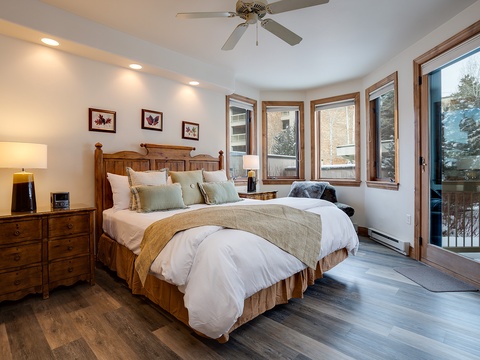 Step into your cozy retreat where warm wood tones and plush bedding invite restful nights. French doors open to your private balcony, framing winter mountain views beyond.
