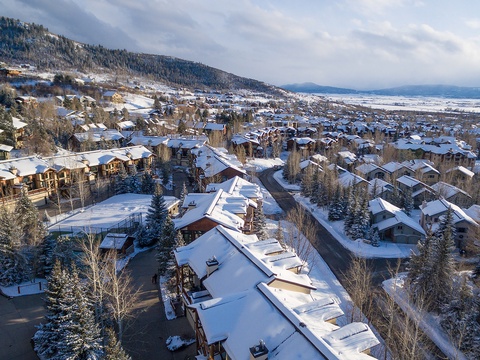 Aerial view of a snow-covered mountain resort community nestled among evergreens, with the valley stretching into the distance under a serene winter sky.