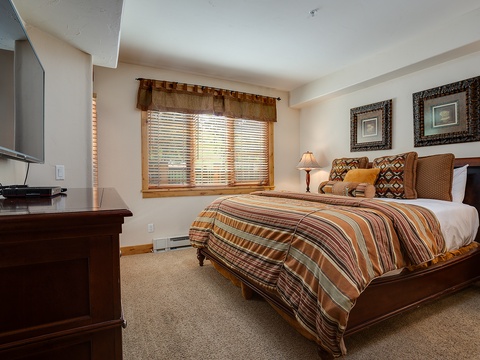 Your cozy bedroom invites restful nights with warm earth tones, a plush bed dressed in southwestern-inspired linens, and natural light filtering through wooden blinds.