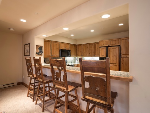 Gather around your breakfast bar with warm wooden seating for four, opening into a fully-equipped kitchen with rich oak cabinetry and modern appliances ready for your mountain retreat meals.