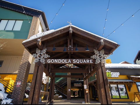 Gondola Square marks the base area entrance, with festive snowflakes and string lights welcoming guests to the mountain village on a crisp winter day.