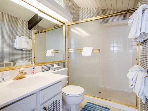 Step into your private bathroom with a sleek glass-enclosed shower, gold-accented fixtures, and plush white towels ready for your arrival.