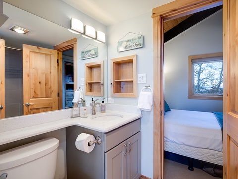 Your private bathroom features natural wood accents, warm lighting, and thoughtful touches like the cheerful wall signs. Step out and sink into a cozy bedroom just beyond the door.