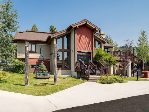 Modern mountain lodge-style building with expansive decks and natural landscaping, providing a welcoming arrival experience in a scenic area.