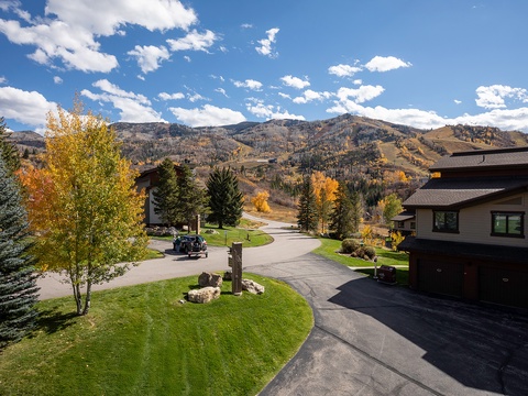 Mountain property exterior features aspen-lined driveway, manicured lawns, and stunning autumn foliage framing the approach to this private vacation rental in a peaceful alpine setting.