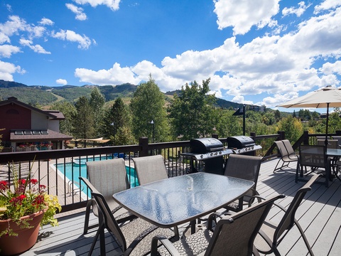 The spacious deck overlooks mountain vistas and a nearby pool, featuring multiple dining areas and twin barbecue grills ready for your outdoor gatherings.