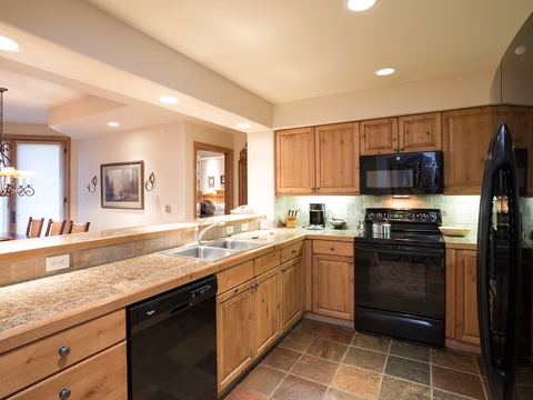 Your fully equipped kitchen features granite counters, warm wood cabinetry, and modern black appliances—perfect for preparing home-cooked meals with everyone gathered around.