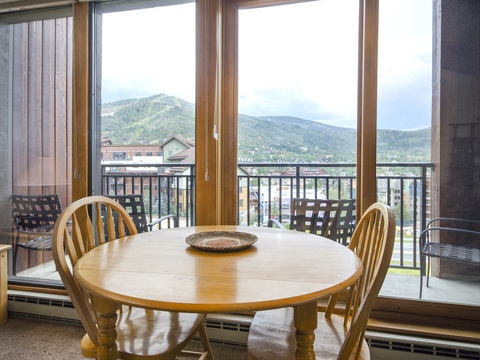 Dining table overlooking majestic mountain vistas through expansive windows, where your morning coffee or evening meal comes with panoramic alpine views and balcony access.