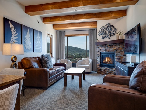 Unwind in your cozy living room with exposed wood beams, a crackling fireplace, and sweeping mountain views that invite relaxation and tranquility.