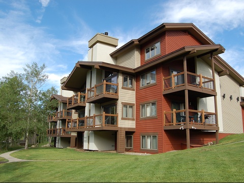 Multi-level vacation property featuring warm-toned architecture with private balconies, set on manicured green lawns surrounded by aspens and mountain views.