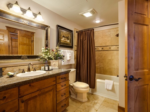 Your private bathroom features warm wood cabinetry, granite countertops, and a relaxing tub-shower combo with elegant tile accents—perfect for unwinding after a day of mountain adventures.