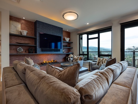 Sink into plush seating while the fireplace glows warmly and the mountain view unfolds through expansive windows—your perfect retreat for cozy evenings.