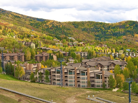 Nestled in a picturesque mountain valley, this seasonal ski resort community features lush autumn foliage, evergreen forests, and lift infrastructure set against dramatic hillside terrain.