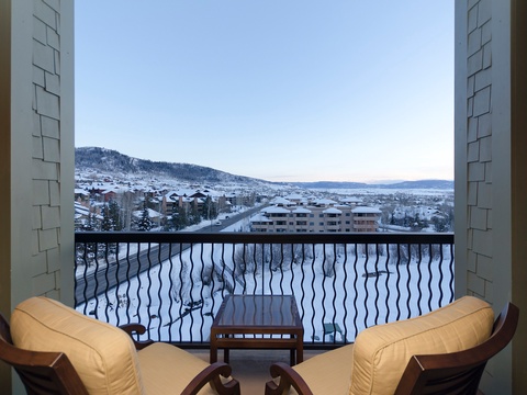 A peaceful winter vista unfolds beyond the balcony, showcasing snow-covered mountain slopes and the surrounding community nestled in the valley below.