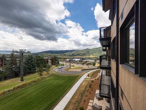 The property sits in a picturesque mountain setting with rolling hills, nearby neighborhoods, and scenic surrounding area visible on approach.