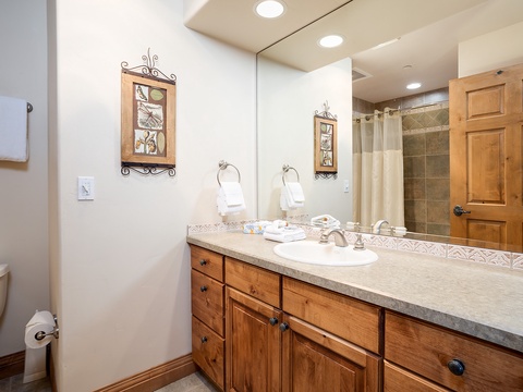 Your private bathroom offers plenty of space to refresh and unwind, with warm wood cabinetry, a spacious vanity, and a tiled walk-in shower waiting just beyond the mirror.