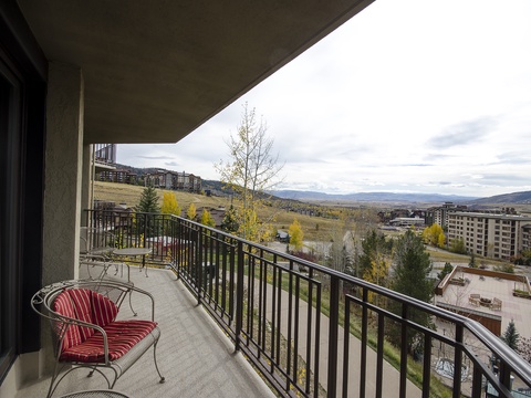 The property sits within a residential area surrounded by rolling hills, autumn-touched trees, and nearby multi-story buildings, offering a peaceful mountain-valley setting.