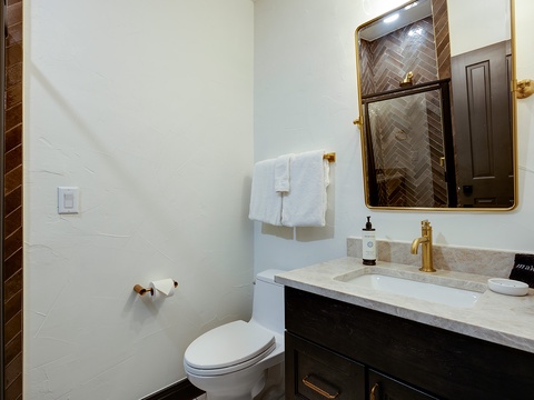 Freshen up in your private bathroom featuring elegant herringbone accents, gleaming gold fixtures, plush towels, and a pristine marble vanity awaiting your arrival.