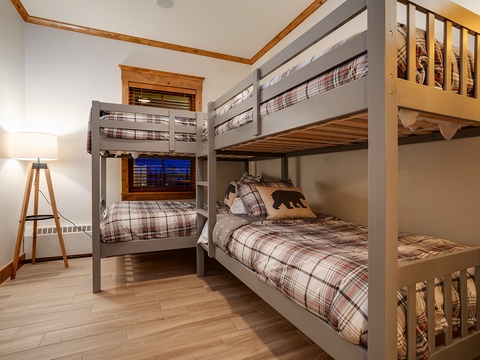 Cozy bunk room with rustic wood accents and plaid bedding invites your group to settle in for restful nights after mountain adventures, all bathed in warm, welcoming light.