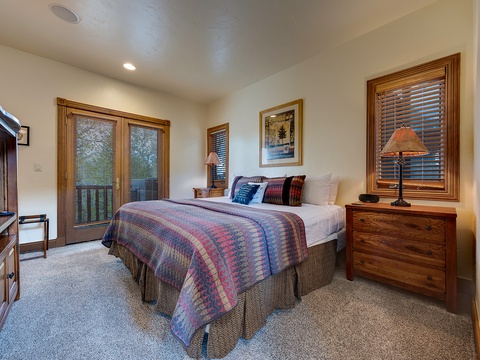Sink into the plush bed dressed with colorful quilts and layers of pillows. Natural light filters through wooden blinds while warm lamps create a peaceful ambiance for your mountain retreat.