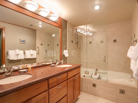 Relax in your spacious bathroom with a deep soaking tub, separate glass-enclosed shower, dual sinks with warm wood cabinetry, and plush towels awaiting your arrival.