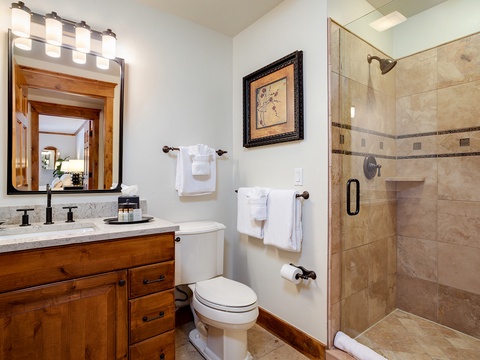 This warm bathroom features travertine tile throughout, a glass-enclosed walk-in shower, modern fixtures, and thoughtful vanity lighting. Fresh white towels await your arrival.
