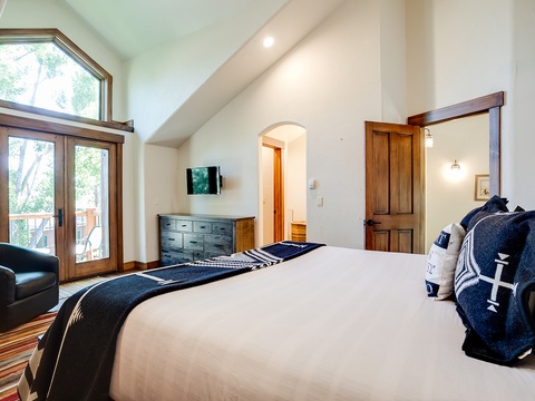Your serene bedroom features vaulted ceilings, warm wood accents, and French doors opening to a private balcony. Sink into crisp linens after exploring the outdoors just beyond.