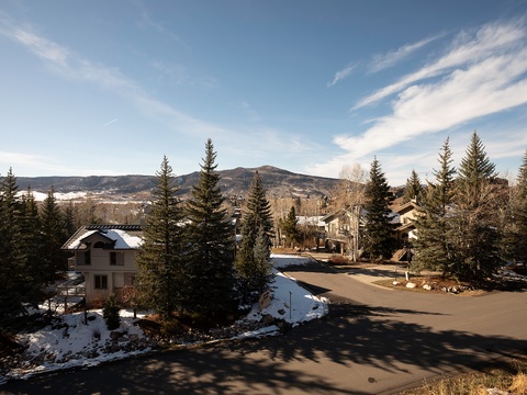 A peaceful mountain community nestled among towering evergreens, with snow-capped peaks visible in the distance and tranquil residential streets below.