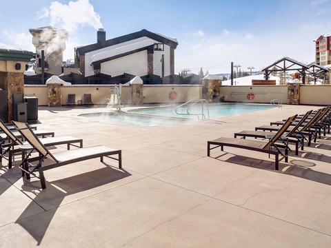 A heated outdoor pool surrounded by sun loungers offers a perfect relaxation spot. Stone columns and mountain views complete this inviting winter retreat.