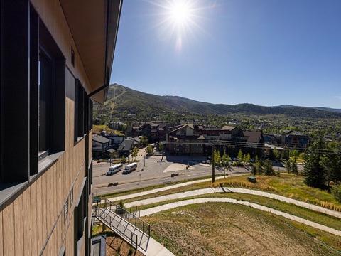 The property sits in a scenic mountain town surrounded by evergreen-covered slopes and a charming neighborhood, with bright blue skies and abundant sunshine overhead.