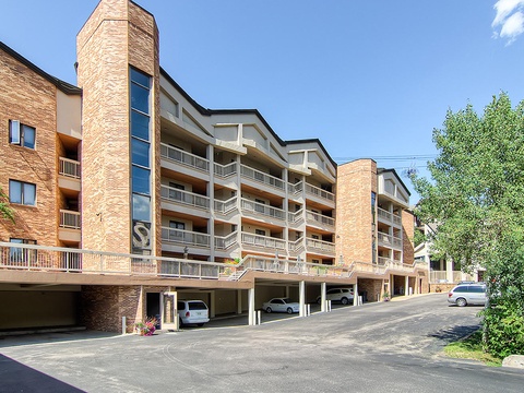 Contemporary multi-story brick building featuring covered parking, private balconies, and modern architectural design set against clear blue skies.
