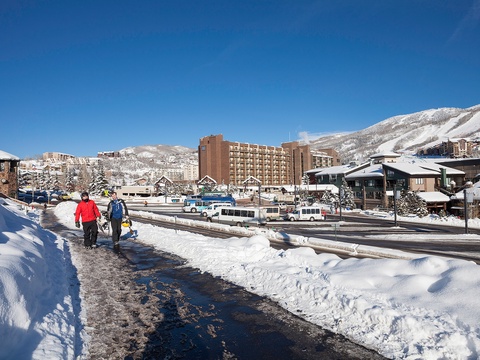 A winter resort town framed by snow-covered mountains, with ski lodges, shuttle buses, and nearby slopes visible—perfect location for a mountain getaway.