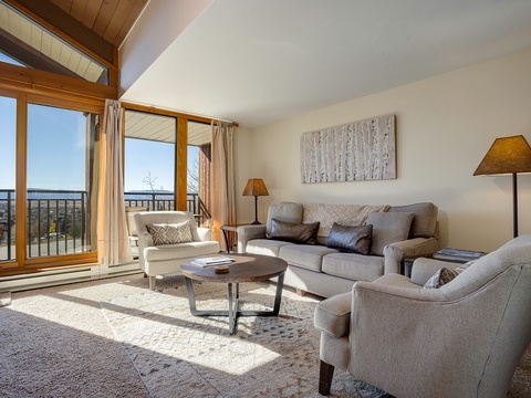 Sink into plush seating as natural light fills your living room, where vaulted ceilings and panoramic balcony views create your perfect mountain retreat.
